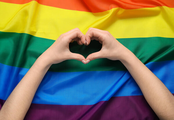 Женщина, создающая сердце руками на флаге ЛГБТ