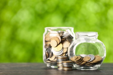 Masada bozuk paralar olan kavanozlar bulanık yeşil doğa arka planına karşı. Tasarruf kavramı