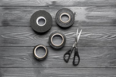 Gri ahşap arka planda yapışkan bant ruloları ve kırtasiye makası