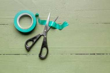 Yapıştırıcı bant rulo ve makas yeşil ahşap zemin üzerinde