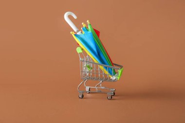 Kahverengi arka planda süpermarket tramvayı ve mini şemsiyeli yaratıcı kompozisyon