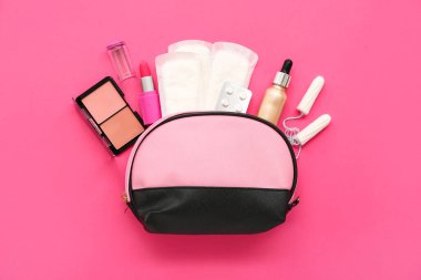 Kadının makyaj malzemeleri, tamponlar ve pembe arka planda regl pedleri olan makyaj çantası.