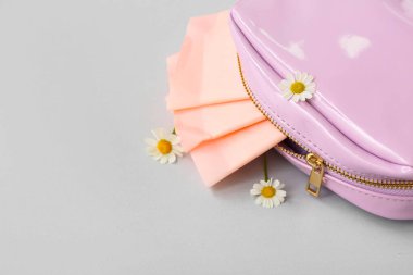 Gri arka planda papatya ve regl pedleri olan bayanın makyaj çantası.