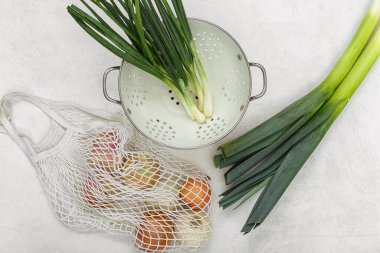 Beyaz arkaplanda farklı soğan çeşitlerine sahip kolander ve ip torbası