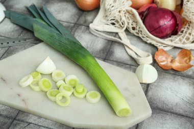 Gri arka planda farklı çeşit soğan içeren tahta ve ip torbası.