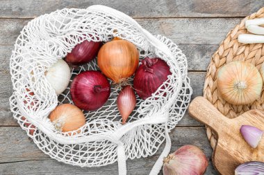 Kahverengi ahşap zemin üzerinde farklı soğan çeşitleri olan tahta ve ip torbaları.