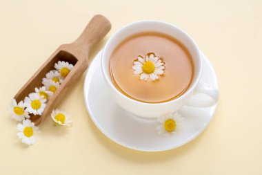 Soluk sarı arka planda kepçeli bir fincan sıcak papatya çayı.