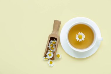 Soluk sarı arka planda kepçeli bir fincan sıcak papatya çayı.