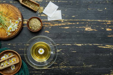 Siyah ahşap arka planda kurutulmuş papatya çayı ve kase.