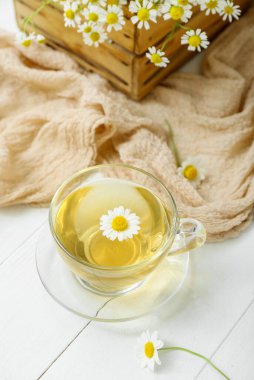 Bir fincan sıcak papatya çayı ve beyaz ahşap arka planda çiçekli kutu.