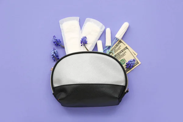 Lady's cosmetic bag with tampons, menstrual pads and money on violet background