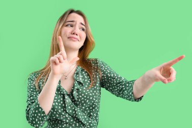 Yeşil arka planda ezik jestleri yapan genç bir kadın.