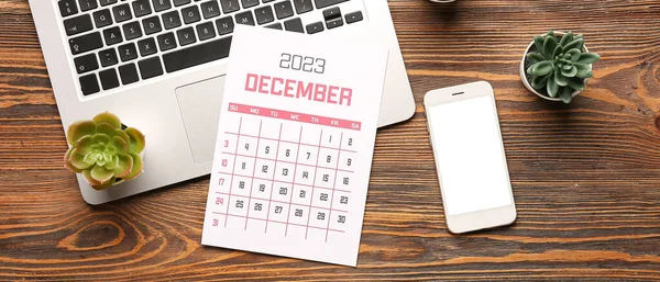 Calendar for December 2023, modern laptop and mobile phone on wooden background