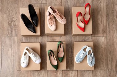 Farklı kadın topuklu ayakkabı ve tahta arka planda spor ayakkabıları olan karton kutular.