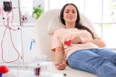 Klinikte uygulamalı tıbbi yaması ve kağıt kalbi olan bir kadın kan bağışçısı.