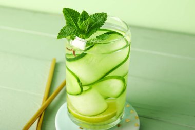 Glass of infused water with cucumber slices on green wooden table clipart