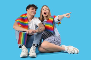 LGBT bayraklı genç çift mavi arka planda bir şeye bakıyor.