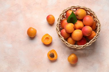 Bej arka planda taze kayısıları olan hasır bir kase.