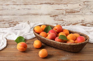 Ahşap arka planda taze kayısıları olan hasır bir kase.