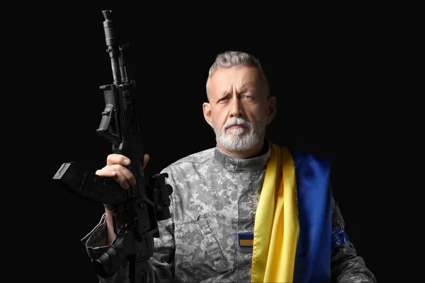 攻撃ライフルと暗い背景にウクライナの旗を持つ成熟した兵士 — ストック写真