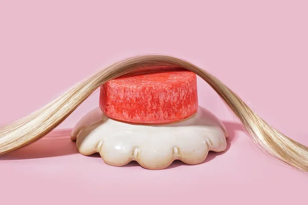 Red solid shampoo bar with hair on pink background