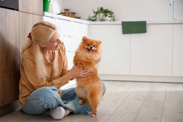 Mature woman with Pomeranian dog in kitchen