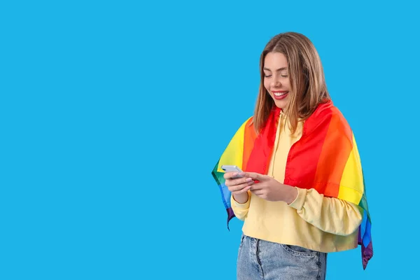 携帯電話を青い背景にLgbtの旗を持つ幸せな若い女性 — ストック写真