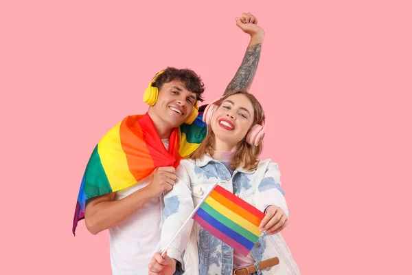 ピンクの背景にLgbtの旗を持つヘッドフォンで若いカップル — ストック写真
