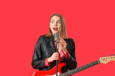 Kırmızı arka planda gitar ve mikrofonlu genç bir kadın şarkı söylüyor.