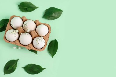Package with Easter eggs, gypsophila flowers and plant leaves on green background
