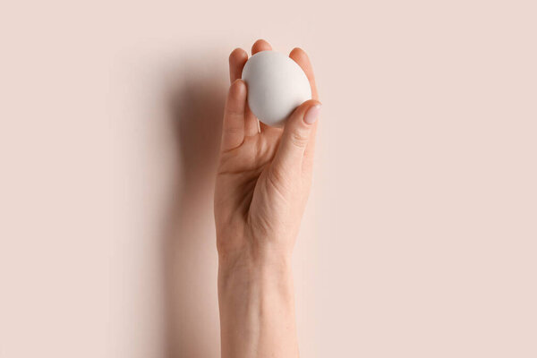 Woman holding egg on beige background