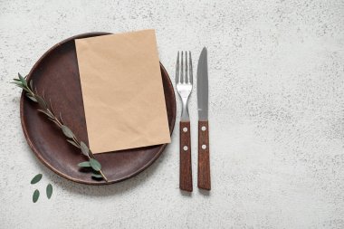 Boş davetiye kartı, çatal bıçak takımı ve beyaz masa üzerindeki okaliptüs dalıyla temiz tabak.