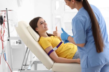 Kadın hemşire klinikte genç bir donörü kan nakline hazırlıyor.