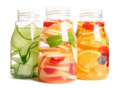 Beyaz zemin üzerinde farklı dilimlenmiş meyvelerle doldurulmuş su şişeleri.