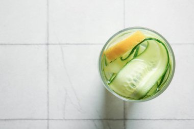 Beyaz seramik zemin üzerinde salatalık dilimleri ile doldurulmuş bir bardak su.