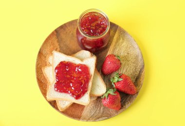 Tahta tabakta tost, lezzetli reçel kavanozu ve sarı arka planda taze çilek.