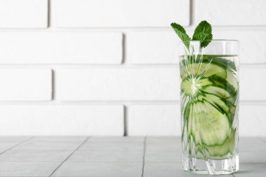 Gri fayans masasında salatalık dilimleri ile doldurulmuş bir bardak su.