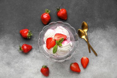 Bir kase vanilyalı dondurma, çilek, nane ve altın kaşıklar gri grunge masasında