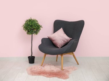 Yastıklı koyu gri koltuk, yumuşak halı ve pembe duvarın yanındaki çiçek.