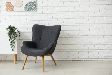 Koyu gri koltuk, şifonyeri, boyası ve beyaz tuğla duvarın yanındaki bitki örtüsü.