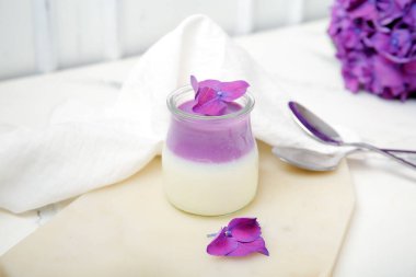 Beyaz masa üzerinde güzel ortanca çiçekleri olan bir bardak panna cotta.