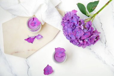 Beyaz masa üzerinde güzel ortanca çiçekleri olan bir bardak panna cotta.