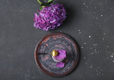 Siyah masanın üzerinde güzel ortanca çiçekleri olan bir bardak panna cotta.