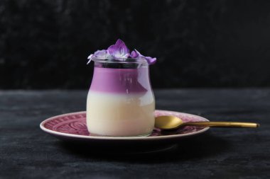 Bir bardak yaban mersinli panna cotta ve siyah masada güzel ortanca çiçekleri.