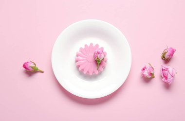 Pembe arka planda güzel gül çiçekleri olan bir tabak panna cotta.