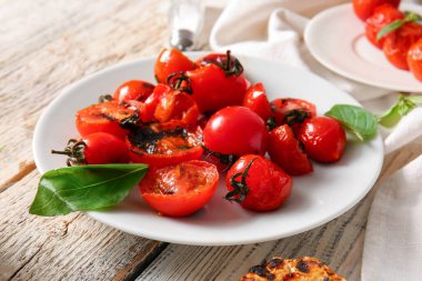 Lezzetli ızgara domates tabakları ve beyaz ahşap arka planda fesleğen.