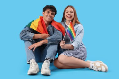 Mavi arka planda oturan LGBT bayraklı genç çift