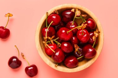 Pembe arka planda taze kirazlı ahşap kase.