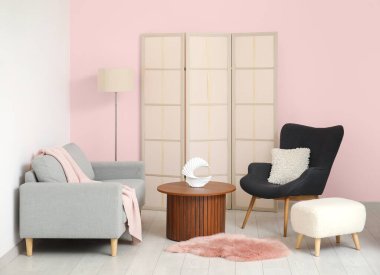 Koltuklar ahşap sehpa, puf ve tuvalet perdesi pembe duvarın yanında.