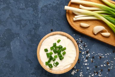 Bir kase lezzetli ekşi krema ve yanında yeşil soğanlı mavi arka plan.